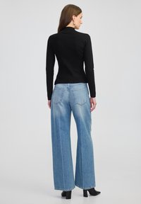 Czarny dopasowany sweter z długimi rękawami w połączeniu ze jasnoniebieskimi spodniami o szerokich nogawkach. Spodnie mają klasyczny pięciopocketowy krój i subtelne przetarcia.