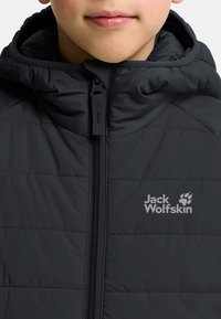 Chaqueta puffer negra con cierre frontal, que cuenta con una capucha ajustada y un logo en el pecho. El material tiene una textura suave y un diseño acolchado.