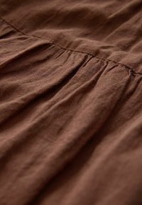 Smeđa tkanina s naboranim šavovima koji stvaraju mekane nabore i teksturu.