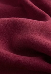 Bordeauxfarbenes Strickgewebe mit einer weichen, strukturierten Oberfläche, das leichten Stretch und einen geschmeidigen Fall aufweist. Nahaufnahme der Faserdetails und des Webmusters.
