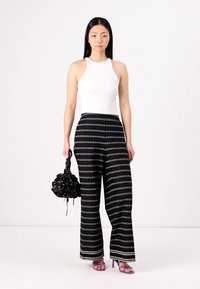 Λευκή αμάνικη μπλούζα, μαύρο παντελόνι wide-leg με γεωμετρικό σχέδιο και μαύρη τσάντα με ρίγες. Το μοντέλο φοράει μωβ ψηλοτάκουνα σανδάλια.