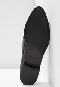 Chaussure habillée en cuir noir reposant sur le côté, semelle tournée vers l'extérieur, montrant l'avant-pointu et la semelle texturée avec la taille 37 marquée.