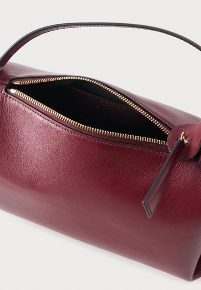 Δερμάτινη τσάντα χειρός σε μπορντό χρώμα με χρυσρό φερμουάρ ελαφρώς ανοιχτό και μικρή λαβή στο ίδιο χρώμα σε λευκό φόντο.