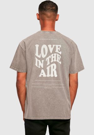 Grå bomulds T-shirt med et stort, hvidt tekstureret grafik, der står "KÆRLIGHED I LUFTEN" på bagsiden, med mindre tekst nedenunder.