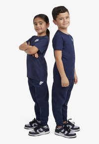 T-shirt in cotone blu navy e pantaloni jogger con loghi Nike bianchi; design aderente; sneakers con accenti neri, grigi e bianchi.