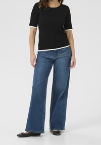 Top corto de manga corta negro con ribete crema, combinado con jeans de pierna ancha azules. El conjunto se completa con bailarinas negras y presenta costuras de mezclilla.