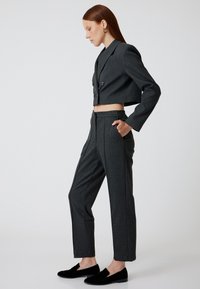 Blazer noir foncé cropped avec double boutonnage, pantalon gris ajusté et chaussures noires sans lacets. Texture lisse, coupe moderne, design minimaliste.