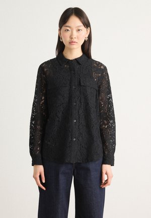 Svart blonder skjorte med lange ermer, knapplukking foran, to brystlommer og intrikate blomster mønstre, kombinert med mørke denim bukser.