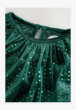 Zelena obleka z nabranim materialom, ki ima sijoče pikaste vzorce in mehak otip. Zapenjanje na hrbtni strani je v obliki ključavnice, material pa je podoben žametnemu.