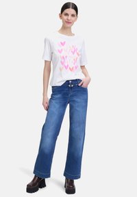 T-shirt blanc avec des graphiques de cœur rose associé à un jean bleu à jambes larges. Bottes à plateforme marron foncé. Tissu lisse et coupe décontractée.