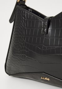 Borsa nera in pelle sintetica con texture a coccodrillo, dal design triangolare e dettagli in metallo dorato. Chiusura con zip sulla parte superiore.