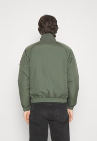 Groene doorgestikte jas met een hoge kraag, elastische zoom en manchetten. Heeft raglanmouwen en een minimalistisch ontwerp. Geschikt voor casual gebruik.