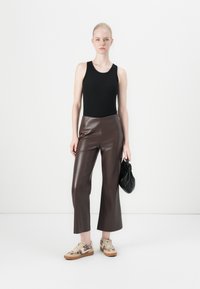 Svart ermeløs topp, brune bukser i imitert skinn med vide ben, mønstrede joggesko med beige og dyreprint, holder en liten svart veske.