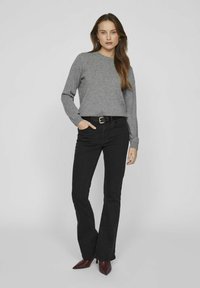 Pilkas megztinis su ilgomis rankovėmis, derinamas su juodais platėjančiais džinsais ir juodu diržu. Modelis dėvi bordo spalvos aštriakulnius batelius.