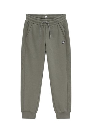 Pantalon de jogging vert olive avec taille à cordon, poches latérales, poignets côtelés, motif matelassé sur les côtés et petit patch avec un geste de la main sur la cuisse.