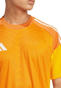 Oranges Sport-T-Shirt mit strukturiertem geometrischem Muster, kurzen Ärmeln und weißen drei Streifen-Akzenten an den Schultern.