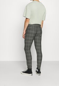 Man som står med ryggen vänd mot oss, iklädd en grön kortärmad skjorta, grå rutig slim-fit byxor och svarta hög-top sneakers.