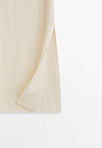 Tissu texturé couleur crème avec un motif géométrique subtil, présenté avec un coin plié sur fond blanc.