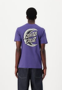 Purple cotton t-shirt featuring a large white and black graphic of a crescent moon with the text "SANTA CRUZ" on the back.