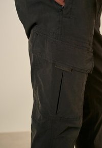 Schwarze Cargo-Hosen aus strapazierfähigem Material, mit Seitentaschen, lockerem Schnitt und dezenten Nähdetails.