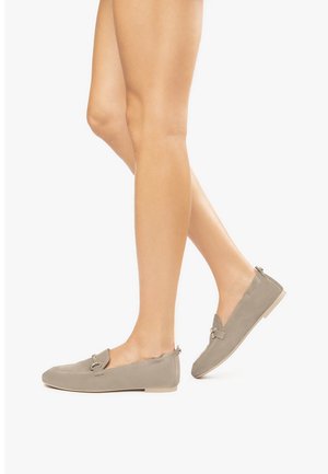 Scarpe slip-on beige con una texture in suede liscia, caratterizzate da un accent metallico decorativo e una suola in gomma beige bassa.