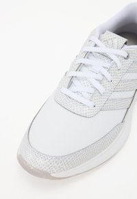 Scarpa sportiva bianca con tomaia in pelle liscia e accenti testurizzati, design con lacci e tre strisce laterali. Suola semitrasparente.