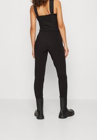 Zwarte jumpsuit met wijde schouderbanden, strakke pasvorm en enkellange benen, gemaakt van een gladde, rekbare stof en met een minimalistische esthetiek.