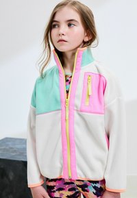 Veste en polaire blanche, vert menthe et rose vif. Dotée d'un col haut, d'une fermeture zippée à l'avant avec des accents jaunes et d'une poche poitrine zippée.