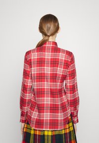 Röd rutig skjorta med krage och långa ärmar, tillverkad av ett lättviktsmaterial med kontrasterande svarta och vita ränder.