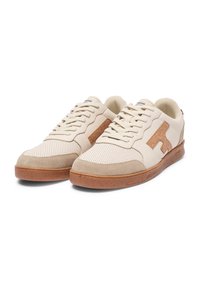 Zapatillas beige con parte superior perforada, acentos de ante y suela de goma marrón. Presentan un logotipo distintivo en el lateral.