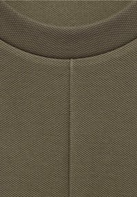 Tissu texturé en vert olive, avec un col rond et une couture centrale dans le dos, mettant en valeur un design structuré.