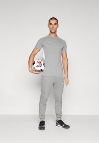 Herren grå treningsantrekk med kortermet topp og smale bukser, laget av et mykt materiale, med hvite detaljer og Puma-logo.