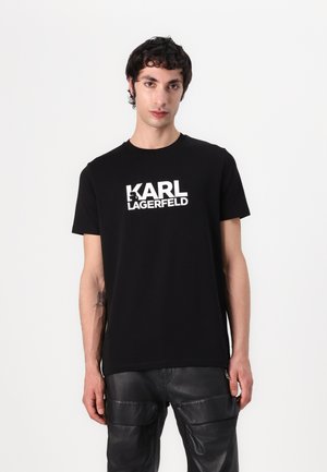 Czarna bawełniana koszulka z białym logo "KARL LAGERFELD" na klatce piersiowej. Projekt z okrągłym dekoltem. Noszona z czarnymi skórzanymi spodniami.