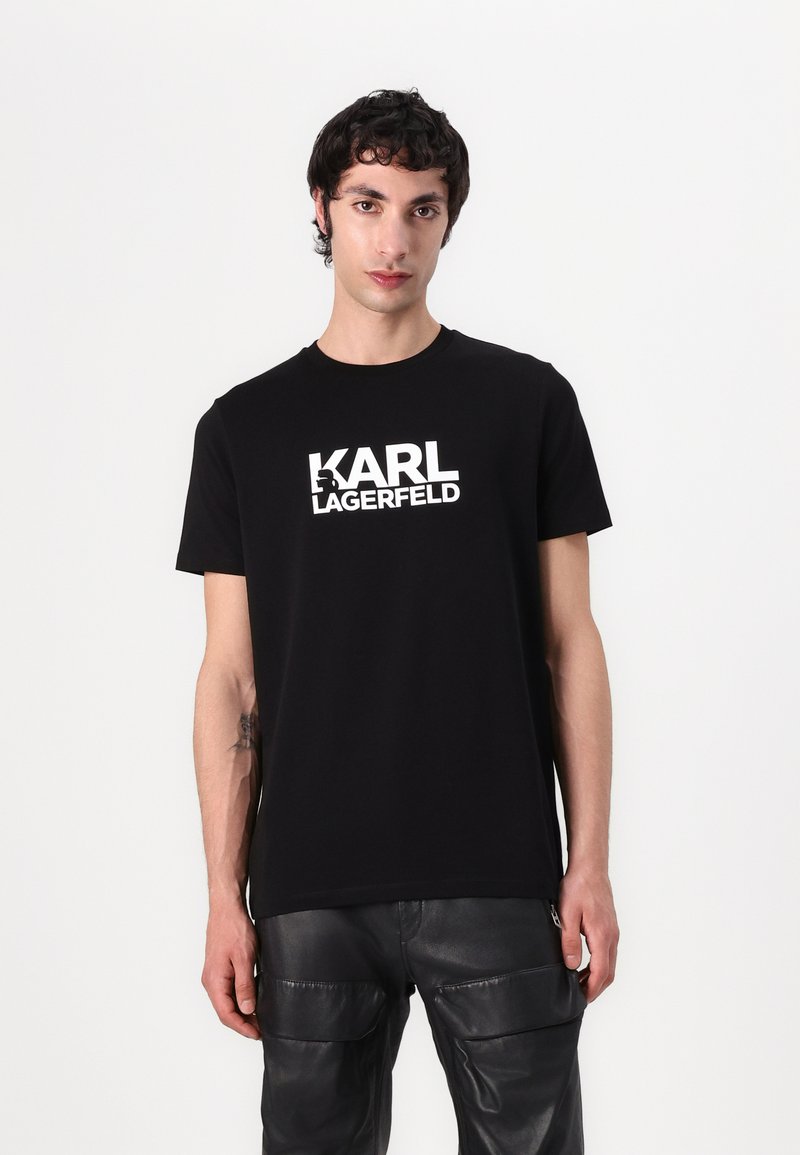 T-shirt en coton noir avec un logo blanc "KARL LAGERFELD" sur la poitrine. Design à col rond. Porté avec un pantalon en cuir noir.
