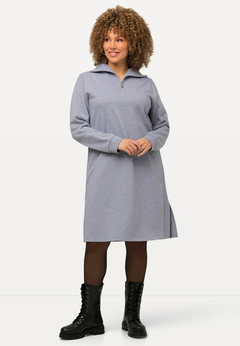 Vestido gris con cremallera, cuello, mangas largas, aberturas laterales y un ajuste relajado. Combinado con botas de combate negras con cordones y medias.