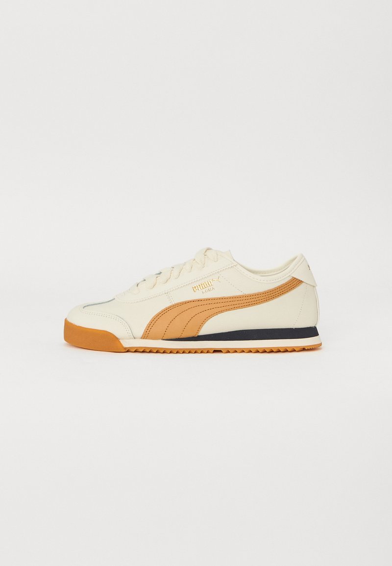 Kremfargede sneakers med oransje detaljer, glatt læroverdel, rund tå og kontrasterende svart såle. Har klassisk snøring og logo.