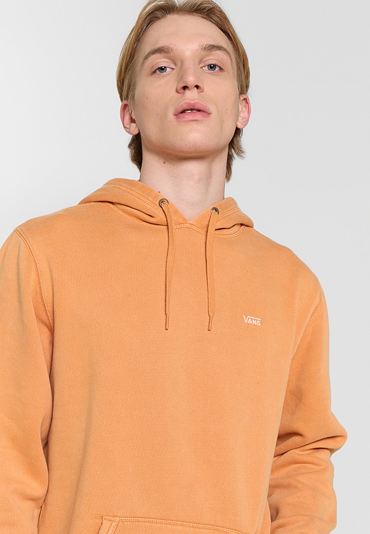 Pfirsichfarbene Vans-Hoodie mit Kängurutasche, Kapuze mit Zugband und Logo auf der Brust. Hergestellt aus weichem Baumwollmischgewebe.