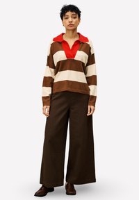 Gestreepte pullover met rode kraag, met brede bruin en crèmekleuren strepen. Gecombineerd met bruine wijde broek en donkere schoenen.