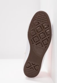 Semelle d'une chaussure Converse All Star blanche montrant un motif en caoutchouc marron avec le nom de la marque embossé.