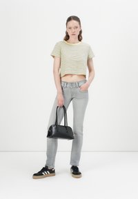 Kuttet gul og hvit stripete t-skjorte, grå tettsittende jeans, svart håndveske med to håndtak, og svarte joggesko med hvite striper.
