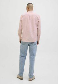Ljust rosa långärmad skjorta med veck bak, knappärmar och rundad nederdel, tillsammans med ljusblå denimjeans och beiga skor.