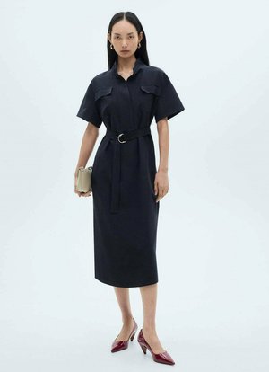 Robe bleu marine à boutons, avec une ceinture, manches courtes, deux poches poitrine et longueur midi ; associée à des escarpins rouges à bout pointu et un sac beige.