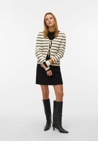 Sweter z dzianiny z czarnymi paskami na kremowym tle, związany z przodu, noszony na czarnej sukience, zestawiony z czarnymi botkami za kolano.