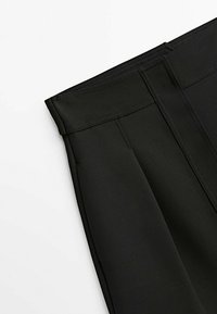 Pantalon noir plissé avec une large ceinture et une texture lisse, présentant des coutures nettes et une coupe ajustée.