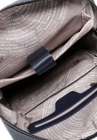 Lõuendist koti sisemus, millel on beež vooder korduvate tekstimustritega, tume rihm ja tasku lukuga sulgemiseks.