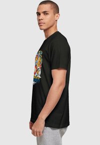 Camiseta de algodón negra con un diseño gráfico colorido en el frontal, que incluye varios personajes y un motivo de ojo prominente.