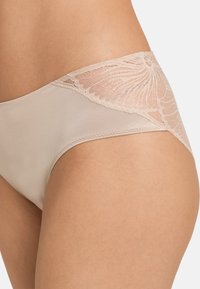 Lingerie beige con un tessuto morbido e dettagli in pizzo su un lato, creando un elemento di contrasto nella texture e nel design.