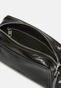 Schwarze Lederhandtasche mit glänzender Textur, ausgestattet mit einem silbernen Reißverschluss und einem geräumigen Innenraum. Glatte Oberfläche mit minimalistischem Design.
