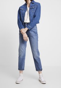 Denim jacket with two chest pockets, light blue jeans, and white high-top sneakers. Casual fit with cropped jacket and rolled hem on pants.