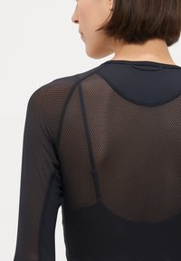 Črna športna majica z dolgimi rokavi z teksturiranim mrežastim vzorcem. Ima okroglo ovratnik in raglan rokave za prileganje oblikovanju.
